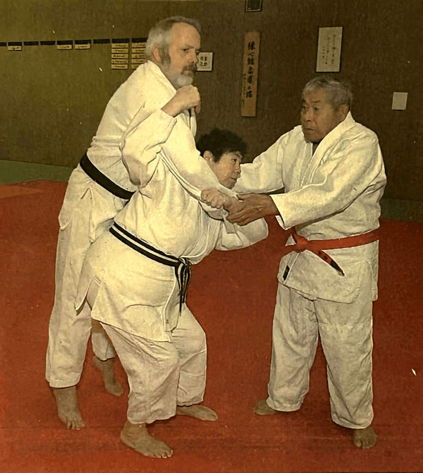 Cutting from newspaper with caption “Sachio Ashida, right, helps his daughter, Janet Ashida Johnson, and her husband, Don, with a Seoi-Nage technique. The 82-year-old, who has just been awarded a ninth-degree black belt by the United States Judo Federation, guided his daughter and son-in-law through the technique recently in the Judo room at SUNY Brockport\'s Cooper Hall. (Photo by Carrie Ann Grippo)”